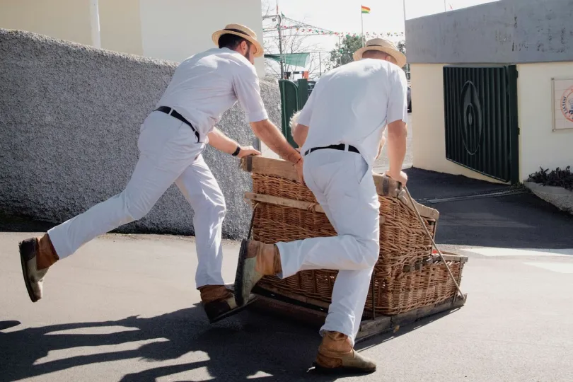 Mannen duwen rieten slee door straten van Funchal. 