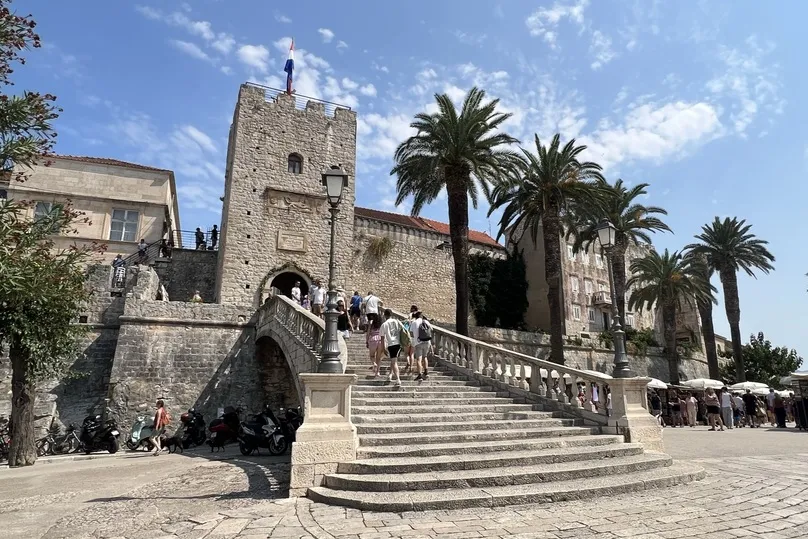 Een historisch gebouw met een grote trap en palmbomen in het centrum van Korcula.