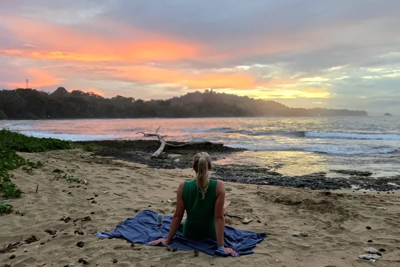 Vrouw zit op een handdoek op het strand in Costa Rica.