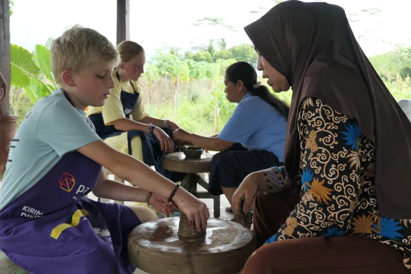 Een kind is samen met een Indonesisch persoon een pot aan het maken.