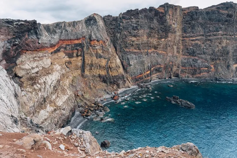 Steile, kleurrijke rotskliffen rijzen op uit het helderblauwe water langs de ruige vulkaankust.