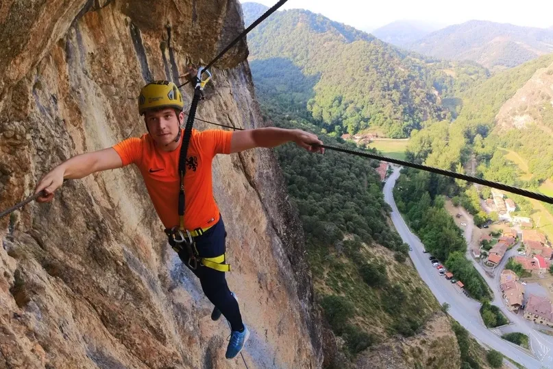 Meneer in Nederlands Oranje t-shirt is een berg vast aan een touw aan het beklimmen.