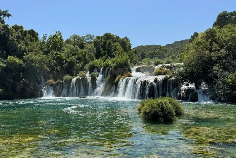 Een waterval tussen de groene bomen en bij een meer.