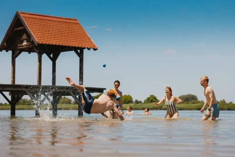 Mensen die een balletje aan het overgooien zijn in laag water. 