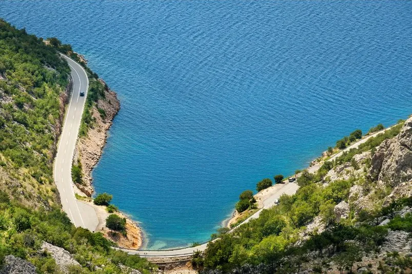 Een lange autoweg die langs de helderblauwe zee gaat.