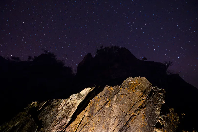 Een rots met een oude tekening erop met erboven een sterrenhemel.
