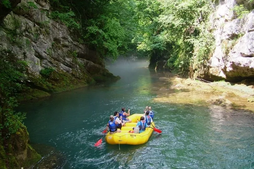 Een grote kajakboot met zes personen erin, op een blauw meer tussen de rotsen.