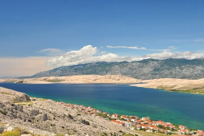 Een blauwe zee met daar langs huisjes, bergen en zandstranden.