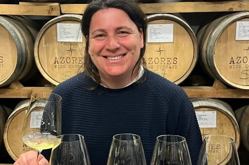 Een vrouw die voor barrels staat met een glas witte wijn. 