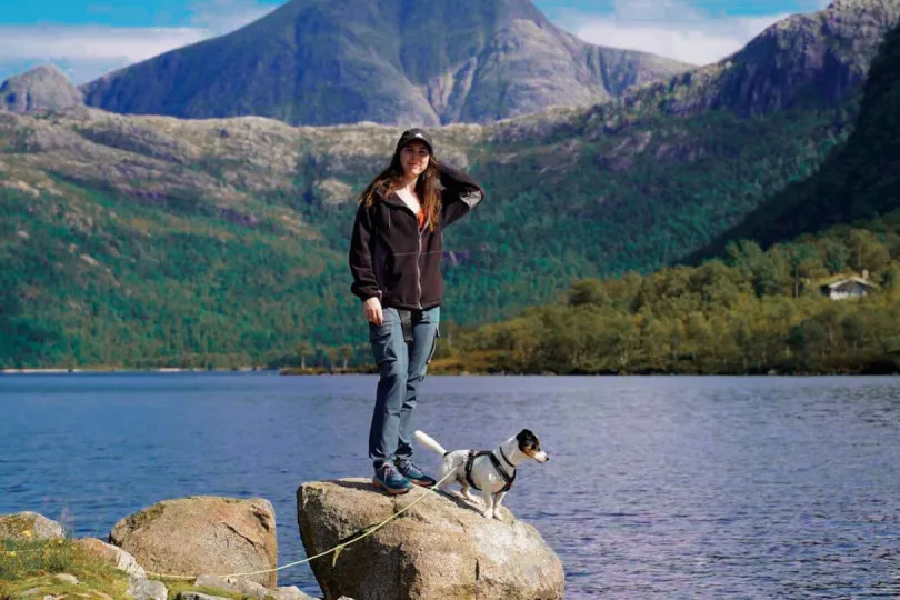 Reisexpert anna samen met haar hond op een rots omringd door water met bergen op de achtergrond.