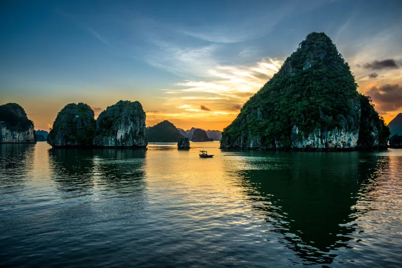 Ha Long Bay bij zonsondergang, met een kleine boot op het rustige water.