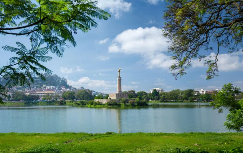 Anosymeer in Antananarivo met monument op een eiland, omringd door groen en bebouwing.