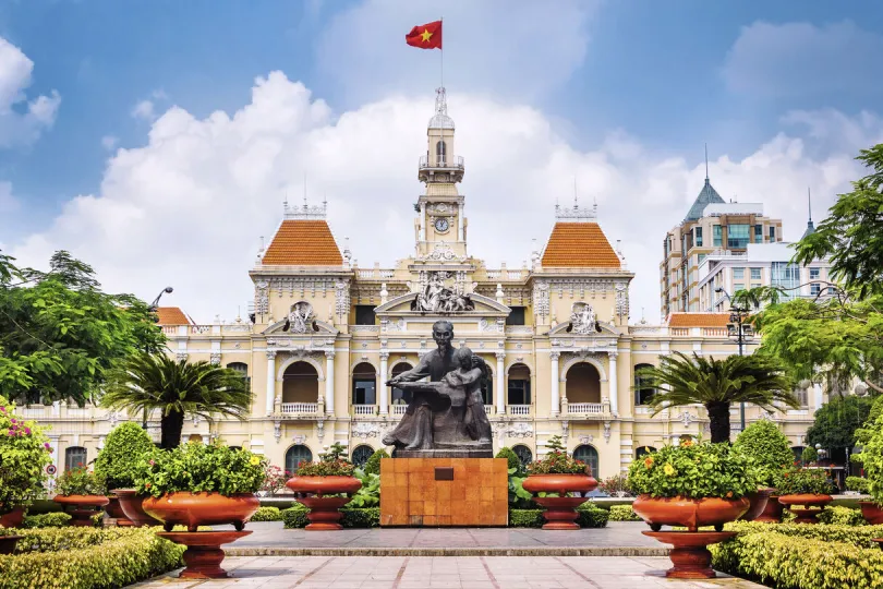Koloniaal stadhuis in Ho Chi Minhstad met een standbeeld en de Vietnamese vlag ervoor.