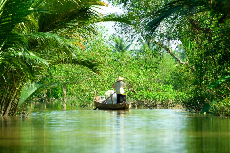Kleine houten boot op een smalle rivier, omringd door groen.