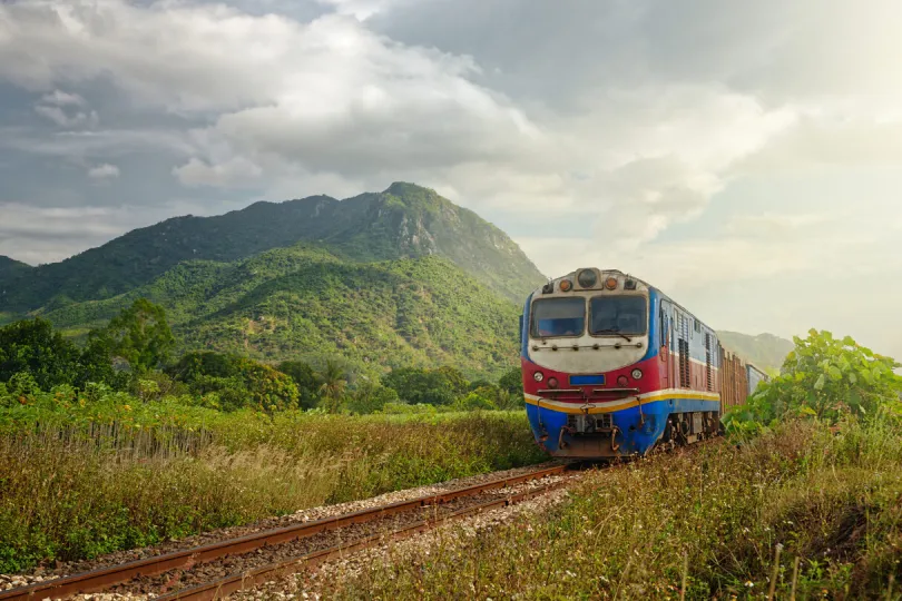 Trein die door een groen berglandschap rijdt, met heuvels en wolken op de achtergrond.