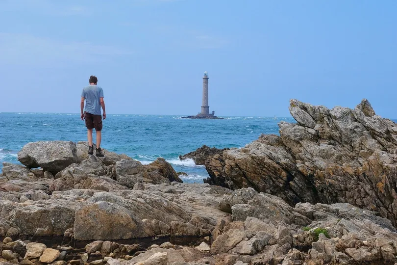Man staat op rotsen en kijkt uit over zee met een vuurtoren.