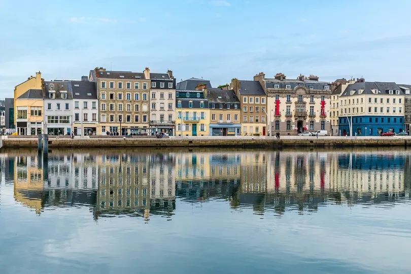 Wandelreis langs de Normandische kust - Uitzicht de kustlijn van de stad Chabourg met reflectie van de stad op het water.