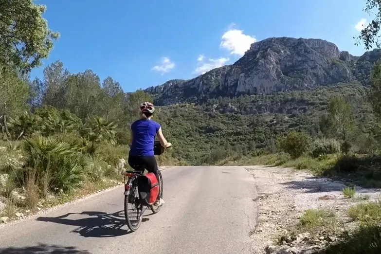 Fietser op de weg met bergen op de achtergrond.