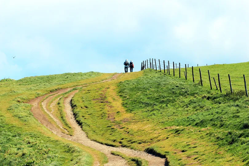 Een koppel wandelt over een groene heuvel in Normandie op een zonnige dag.