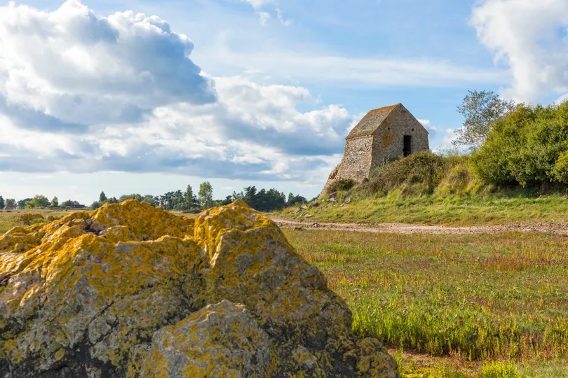 Een kleine stenen kapel in een groen grasland met een pad door het midden en wat rotsen.
