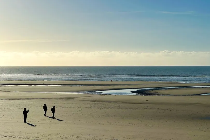 Wijdt zandstrand waar de zon ondergaat en er lopen een paar mensen op het strand.