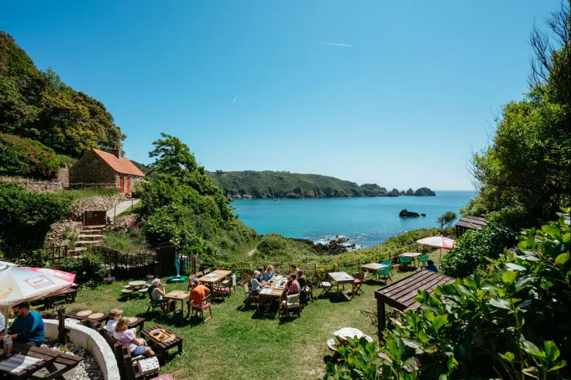 Praktische info kanaaleilanden, Terras met uitzicht op een turquoise baai en rotsachtige kust op de Kanaaleilanden.