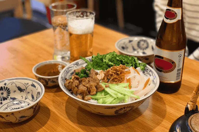 Vietnamese noedelkom met gegrild vlees, groenten en bier op tafel.