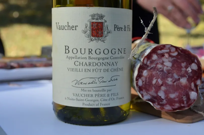Bourgondische chardonnay ingezoomd op het wijnetiket die op tafel staat naar een opengesneden worst.