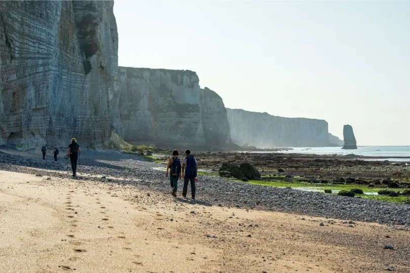 Wandelaars lopen over een strand langs de kliffen in Normandië op een zonnige dag.