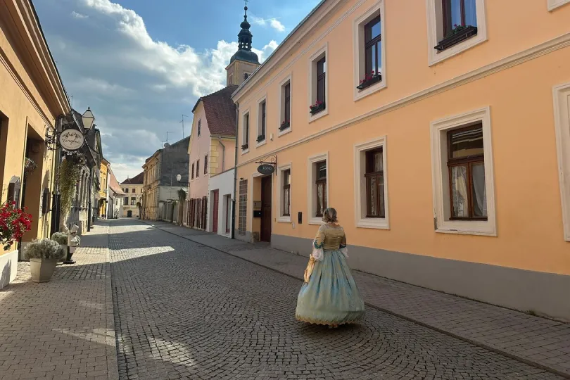Een vrouw loopt door een straat met kleurrijke gebouwen en een kerktoren.