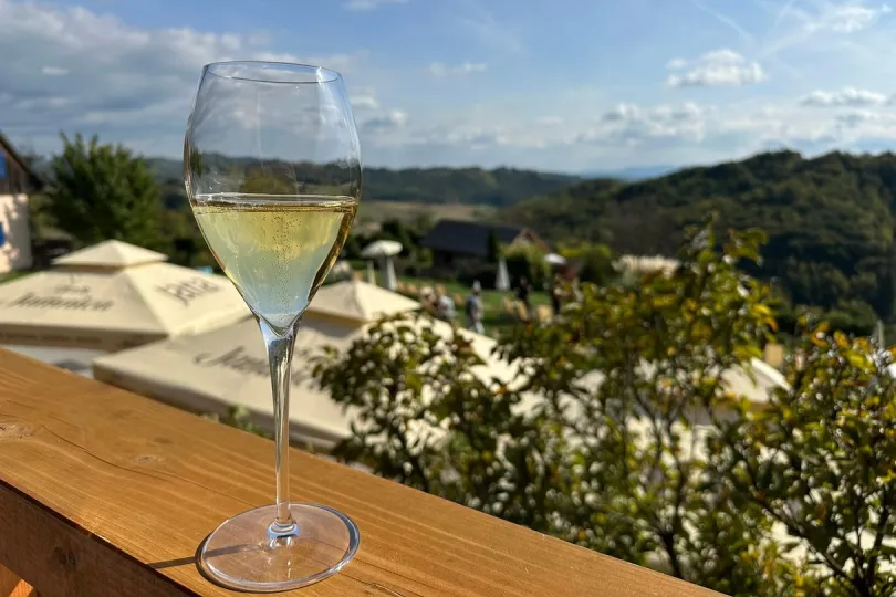 Een glas witte wijn staat op een tafel met uitzicht op groene heuvels.