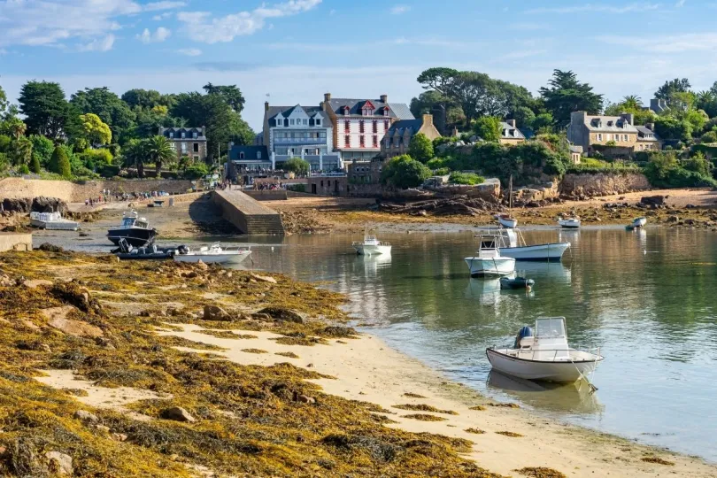 Een met zeewier bedekt strand bij het eiland Bréhat in Bretagne, met in het water een aantal bootjes.