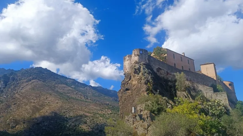 Uitzicht op de top van een berg in Corsica bij het stadje Corte waarbij je opkijkt naar de Corte citadel op een top van een berg met groene bomen.