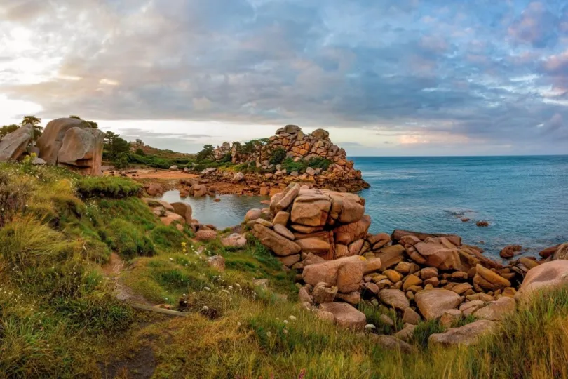Beeld van mooie natuur aan de Roze Granietkust van Bretagne, met links een heidelandschap en rechts grote rotsblokken aan de blauwe zee.