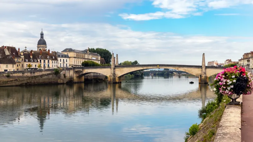 Chalon-sur-Saône in Frankrijk met uitzicht op een oude stenen brug met aan de ene kant een mooie pot met prachtige bloemen erin en aan de andere kant een stadje waarbij de kerktoren boven de gebouwen uitsteekt.