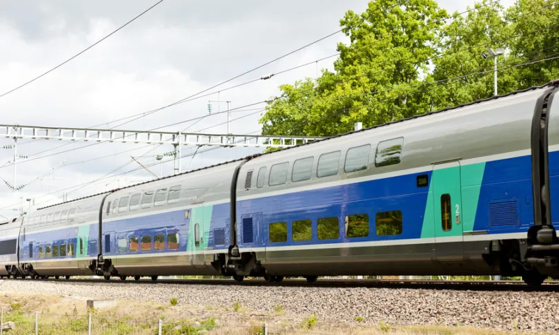 Groen, grijs, blauwe TGV trein in Frankrijk die voorbij rijdt met daarachter een groene grote boom.