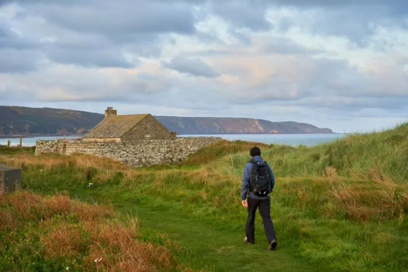 Een wandelaar loopt langs de kust van Normandië en passeert een stenen huisje.