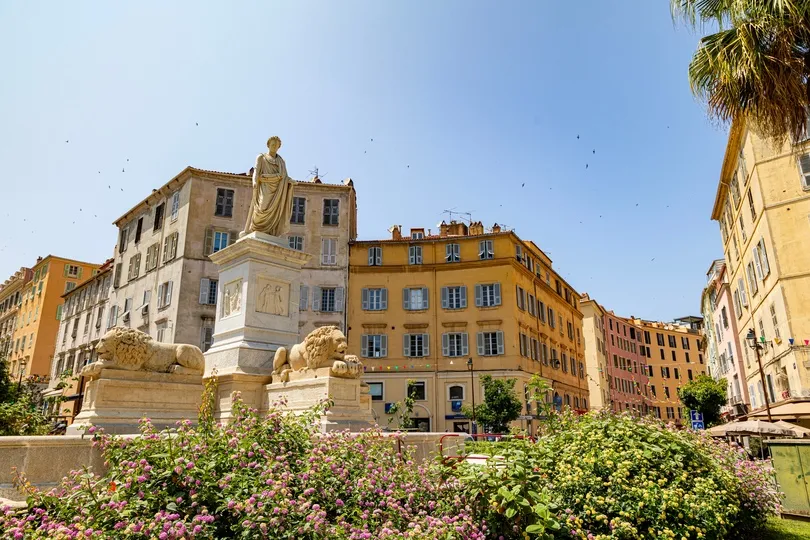 Een sfeervol stadsplein met een standbeeld, kleurrijke bloemen en historische gebouwen vormt het hart van het zonnige Ajaccio.