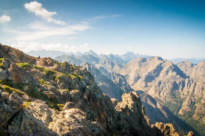 Een indrukwekkend berglandschap met steile rotsen en diepe dalen strekt zich uit onder een heldere blauwe lucht.