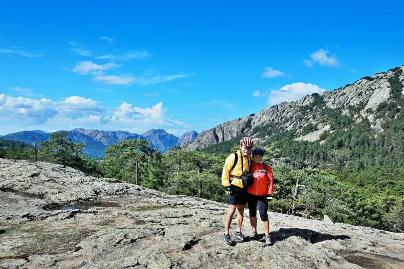 Een vrouw en een man die samen op een rots staan voor een mooi uitzicht over bergen en groene bossen. 