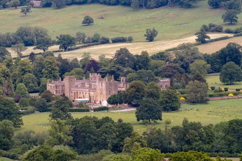 Een historisch kasteel ligt midden in een groen landschap met bossen en weilanden.