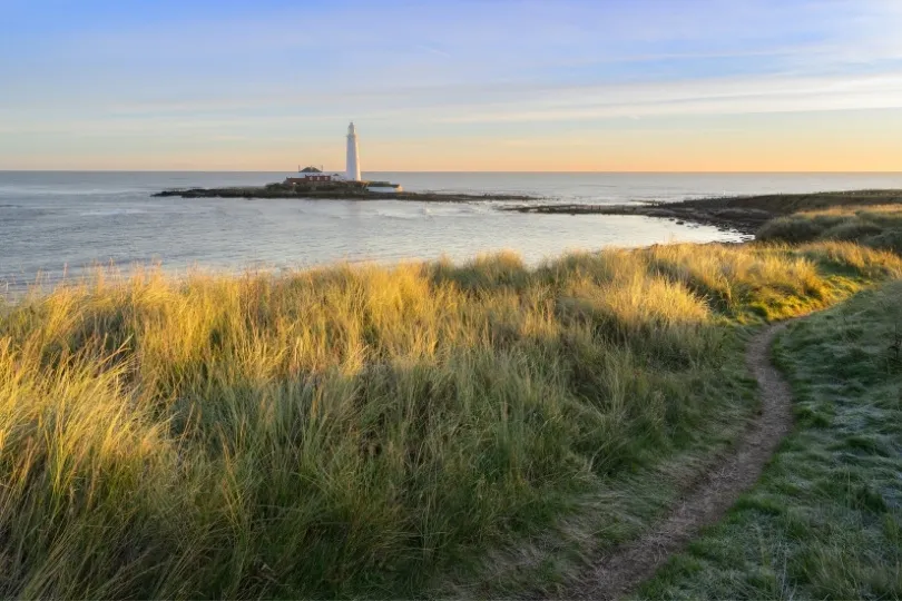 Een kustpad door de duinen leidt naar een vuurtoren aan zee.