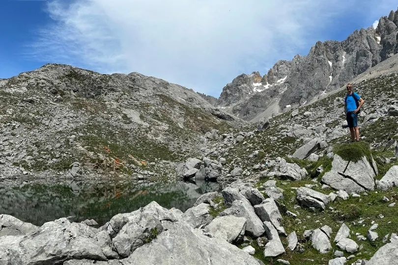 Een wandelaar staat bij een bergmeer, omringd door hoge rotsen en ruige bergtoppen.