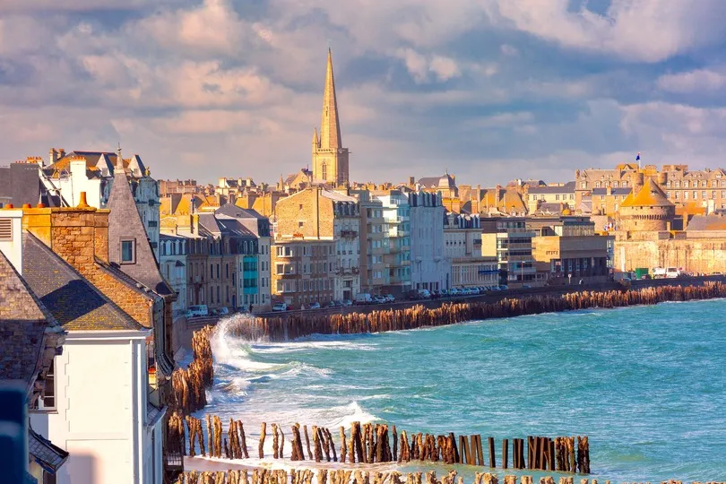 Kuststad Saint Malo met een kerk en blauwe zee die opbotst tegen de kustrand.
