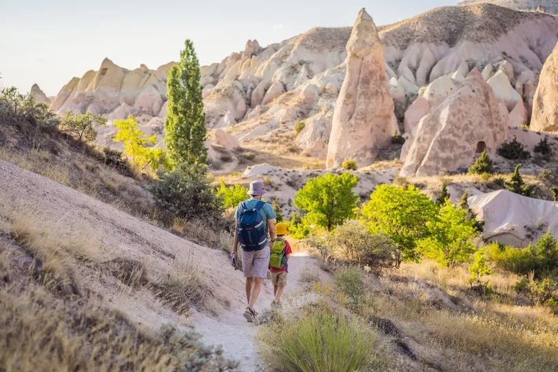 Wandelaar met kind die wandelt door Cappadocië tussen groene bomen.