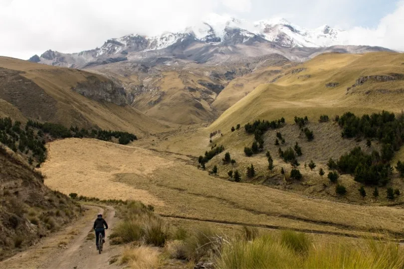 Man op een mountainbike over de flanken van de Chimborazo met bergen op de achtergrond.