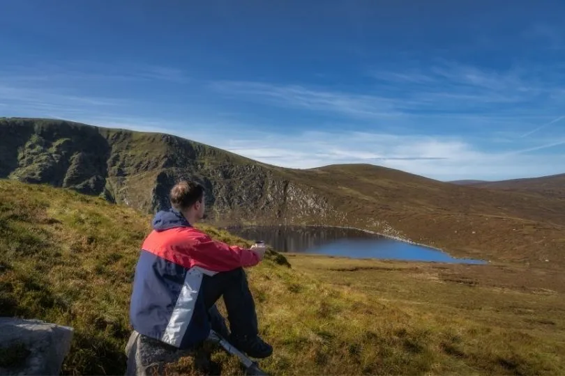Zittende man die uitkijkt naar een berg meer tussen de bergen van Wicklow.