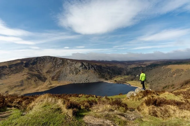 Man die op een steen staan met weids uitzicht over Lough Tay Lake in Ierland.