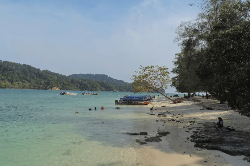 Uitzicht op het strand van Langkawi met helder water en bootjes en mensen in het water.