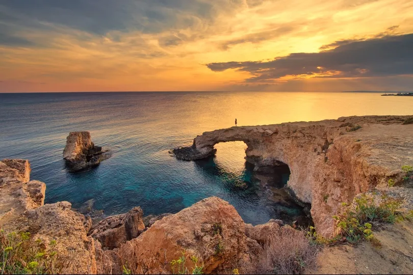 Reiziger staat op een rots tijdens de zonsondergang op Cyprus.